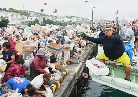 船から陸へカツオの切り身を振りまく漁師　ゲットしようと段ボール箱を抱えて群がる人々　沖縄・伊良部島の海神祭で「大盤振る舞い」